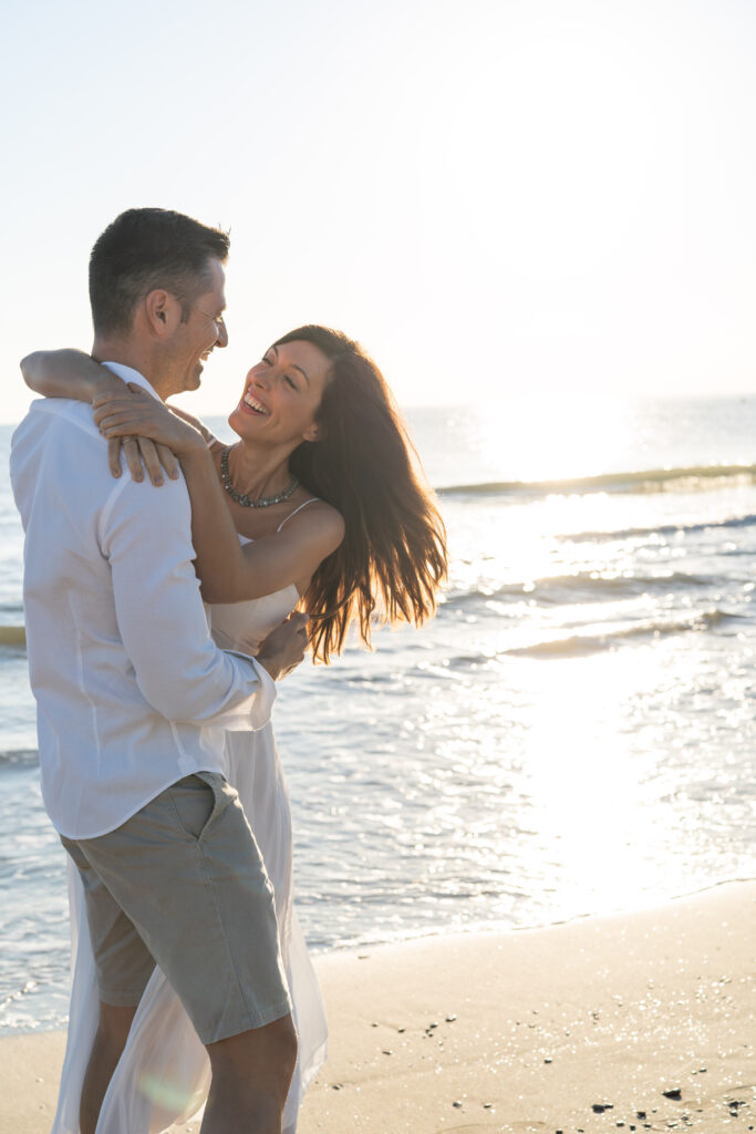 Pareja abrazada y riendo en la orilla de La Patacona, Valencia, iluminados por la luz suave del amanecer.