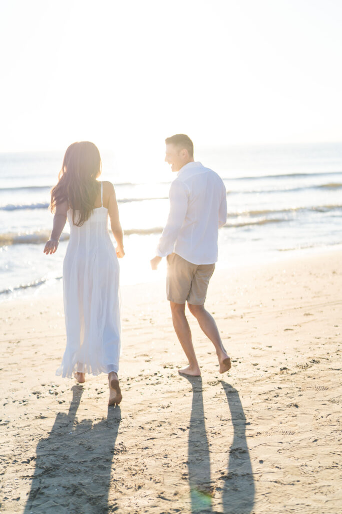 Hombre y mujer caminando descalzos en la arena de La Patacona, Valencia, al amanecer, con luz cálida y suave.