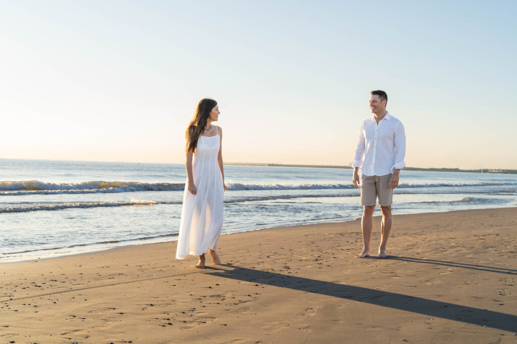Pareja caminando de la mano en la playa La Patacona, Valencia, disfrutando del amanecer y la luz suave del sol.