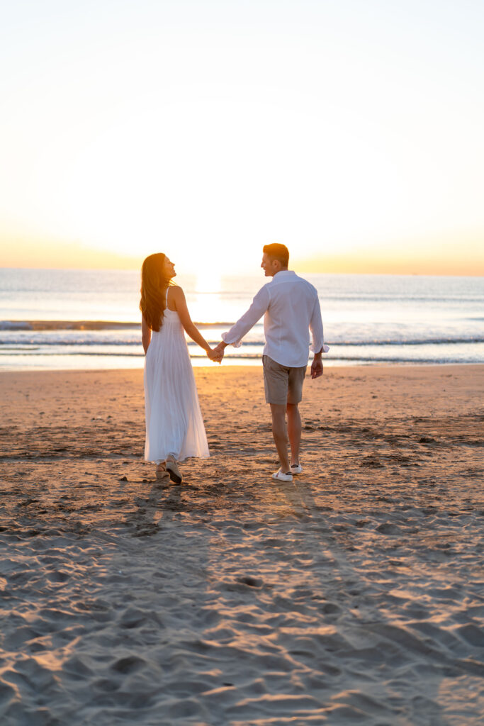 Pareja en la playa La Patacona, Valencia, disfrutando de amor y diversión al amanecer, con luz natural suave y cálida.